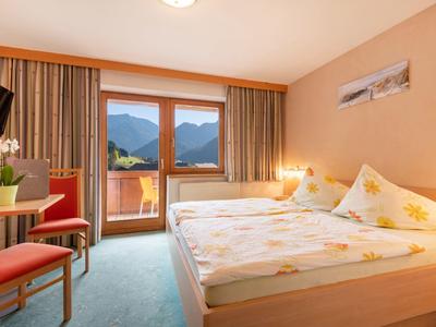Gemütliches Hotelzimmer mit Doppelbett, Balkon, Bergblick, Stühlen und hellem Holzmöbel.
