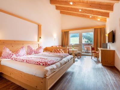 Helles Schlafzimmer mit Holzbalkendecke, großem Bett, Teppichboden und Bergblick durch Fenster.