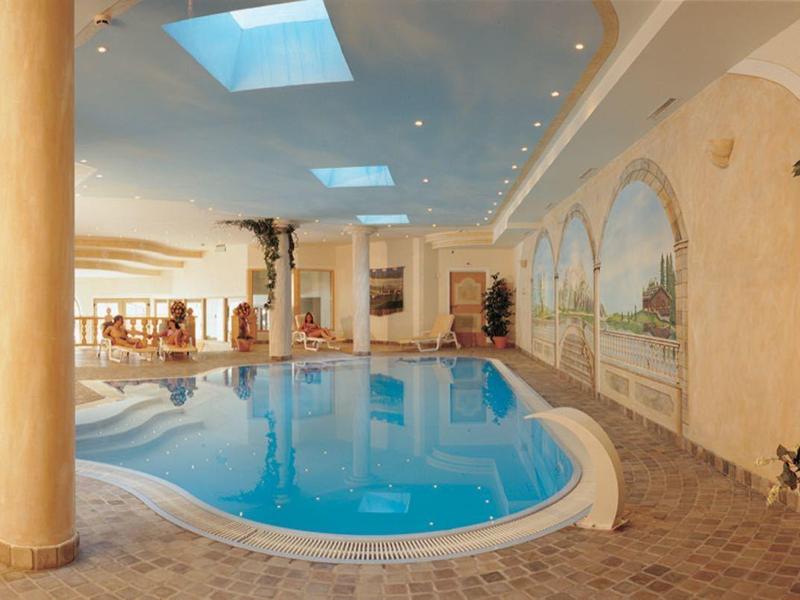 Innenhallenschwimmbad mit blauem Wasser, Säulen, Pflanzen und warmen Beleuchtungselementen.