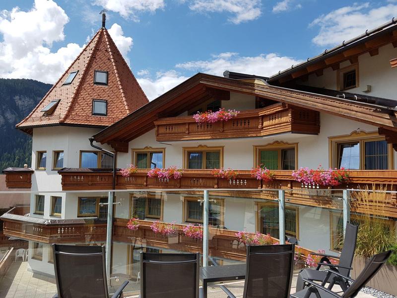 Traditionelles Holzhaus mit Balkon und Blumen vor bergigem Himmel im Dorf.