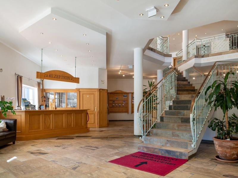 Heller Empfangsbereich mit Holztheke, grünen Pflanzen und moderner Treppe mit Glasgeländer.