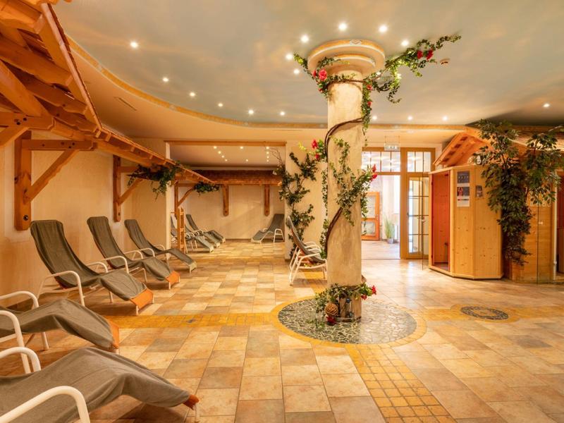 Innenraum eines Wellnessbereichs mit Liegestühlen, Säule mit Pflanzen und warmem Licht.