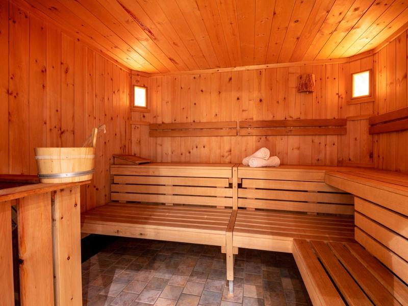 Gemütliche Sauna mit holzverkleideten Wänden, Bänken, Leuchtelementen und einem Holzeimer.