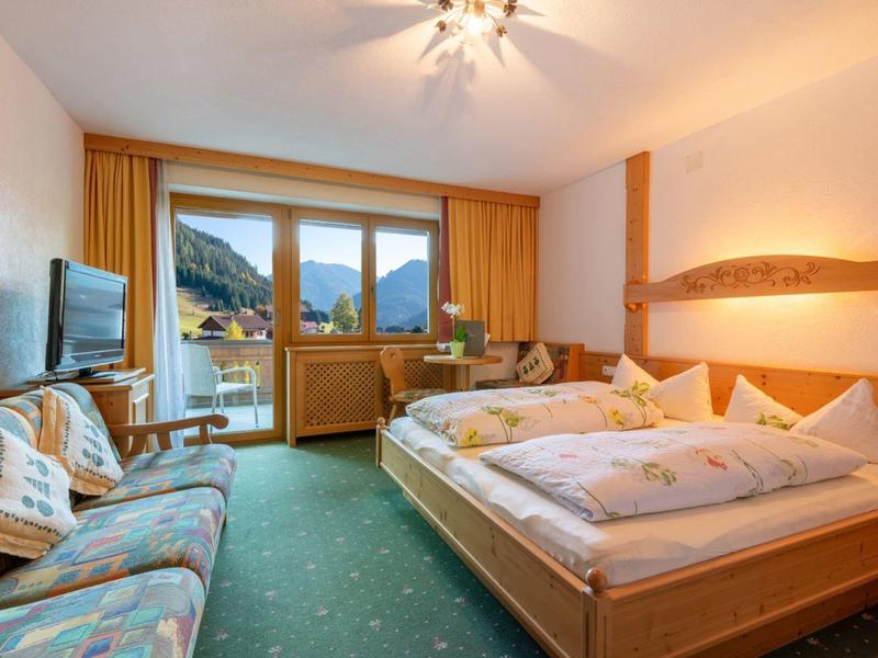 Gemütliches Schlafzimmer mit Holzmöbeln, grünem Teppich und Bergblick durch großes Fenster.