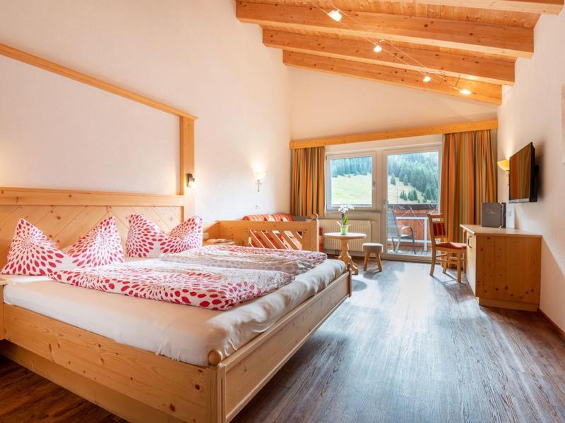 Helles Schlafzimmer mit Holzbalkendecke, großem Bett, Teppichboden und Bergblick durch Fenster.