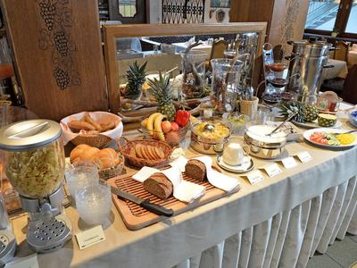 Buffet mit frischem Brot, Croissants, Obst, Müsli und Kaffeeservice in hellem Raum.