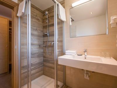 Helles Bad mit Dusche aus Glas, großem Spiegel, Waschbecken und Holztür im Hintergrund.