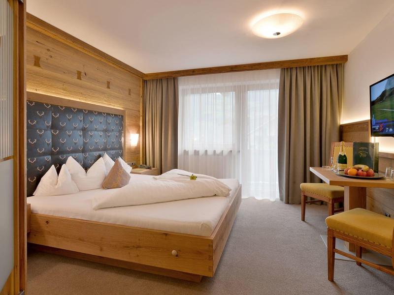 Gemütliches Schlafzimmer mit Holzmöbeln, großem Bett, Fernseher und Fenster mit Gardinen.