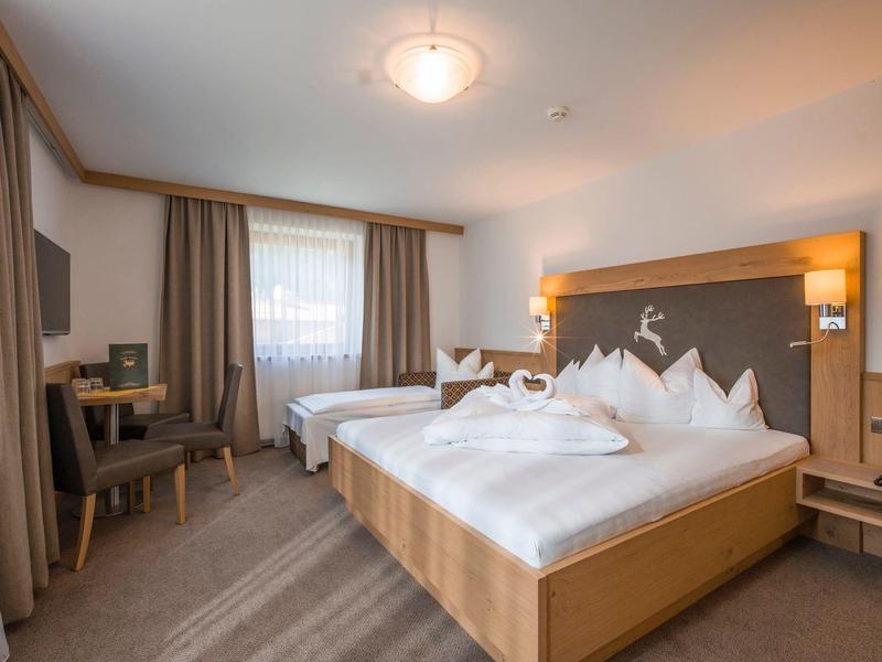 Helles Hotelzimmer mit zwei Betten, Holzmöbeln, Vorhängen und modernen Wandleuchten.