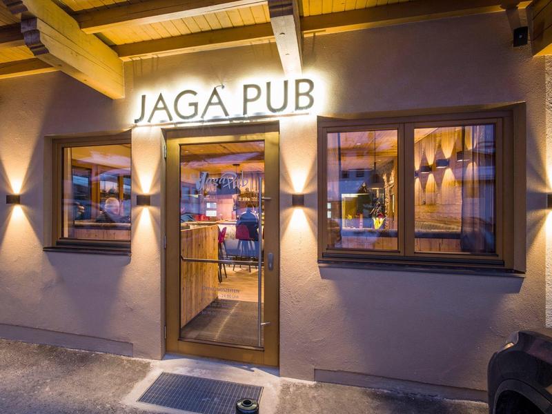 Beleuchteter Pub-Eingang mit zwei Fenstern und Glas-Tür, warme Wandbeleuchtung, Abendstimmung.