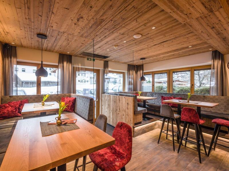 Gemütlicher Gastraum mit Holzdecke, roten Stühlen, großen Fenstern und rustikaler Einrichtung.