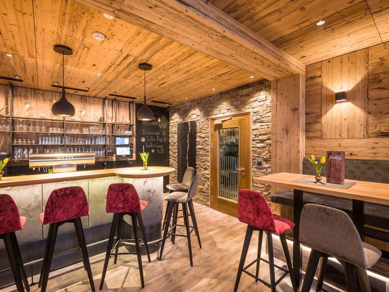 Gemütliche Bar mit Holzwänden, roten und grauen Barhockern sowie stilvollen Pendelleuchten.