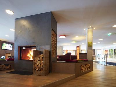 Moderner Wohnzimmerbereich mit Kamin, Holzlager, Holzboden und großen Fenstern für viel Licht.