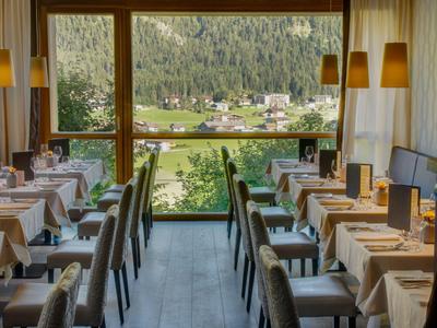 Elegantes Hotelrestaurant mit gedeckten Tischen und Blick auf grüne Landschaft und Dorf.