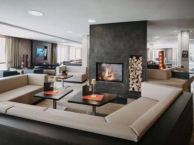 Modernes Hotel-Lounge mit Sofas um einen zentralen Kamin und großem Fenster mit Aussicht.