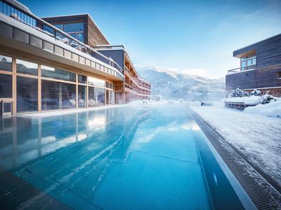 Außenpool zwischen modernen Gebäuden, umgeben von Schnee und Bergen bei klarem Himmel.