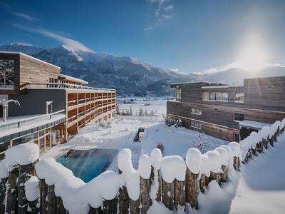 Hotelresort im verschneiten Berggebiet mit Außenpool und Holzbauten unter klarem Himmel.
