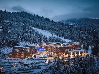 Hotel in verschneitem Bergwald bei Abenddämmerung mit beleuchteten Fenstern.