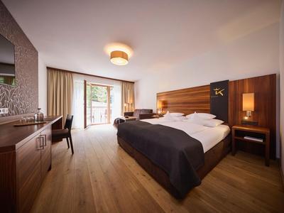 Modernes Hotelzimmer mit Doppelbett, Schreibtisch, Fernseher und Zugang zu einem Balkon.