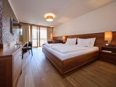 Modernes Hotelzimmer mit großem Bett, Holzmöbeln und Balkon mit Blick auf die Landschaft.