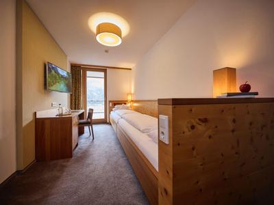 Gemütliches Hotelzimmer mit Holzmöbeln, Einzelbett, Schreibtisch und Balkon mit Bergblick.