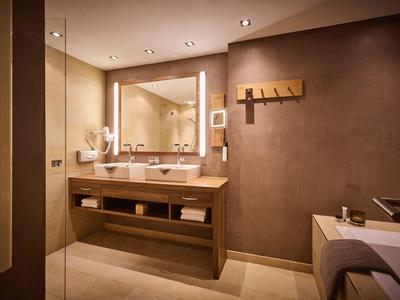 Modernes Badezimmer mit Holzwaschtisch, großem Spiegel und warmen, braunen Farbtönen.