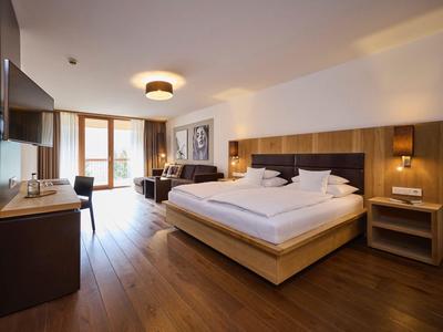 Modernes Hotelzimmer mit Doppelbett, Holzboden, Schreibtisch und großem Fenster mit Tageslicht.