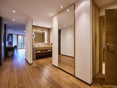 Flur mit Holzboden führt zu Bad und Wohnzimmer in modernem Hotelzimmer.