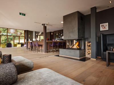 Moderner Hotel-Loungebereich mit Holzboden, Sitzgelegenheiten und zentralem Kamin.