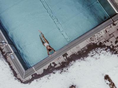 Vogelperspektive eines Schwimmers in einem rechteckigen Außenpool mit Schnee drumherum.