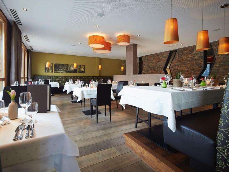 Eleganter Speisesaal mit weißen Tischdecken, Holzboden und warmen Pendelleuchten.