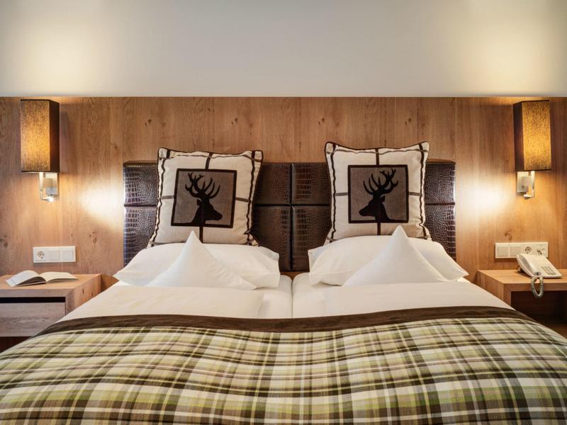 Modernes Hotelzimmer mit Doppelbett, kariertem Bettüberwurf und Hirsch-Motiv-Kissen.