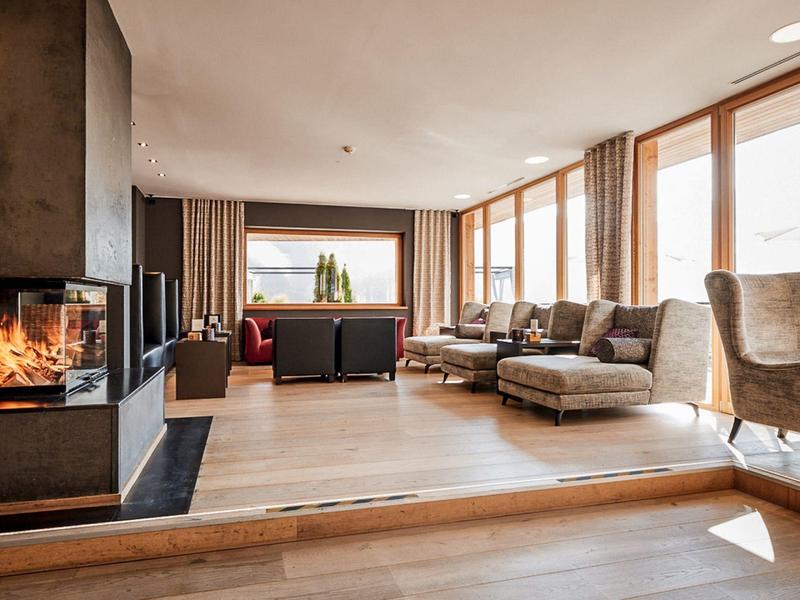 Geräumiges Wohnzimmer mit großen Fenstern, Kamin, hellen Holzböden und modernen, bequemen Möbeln.