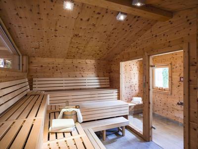 Holzsauna mit Sitzbänken, Eimer, Schöpflöffel und Blick auf angrenzenden Raum.