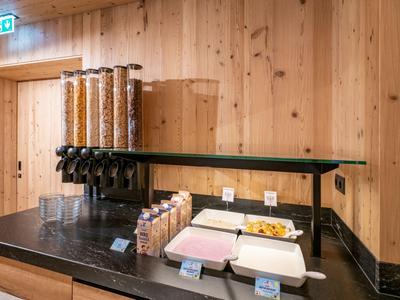 Buffetstation mit Getreidespendern und Brotauswahl an einer Holzverkleideten Wand.