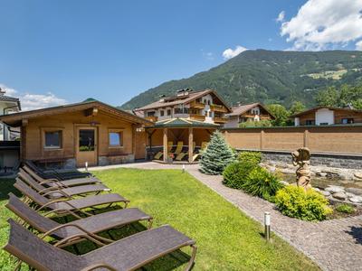 Gartenbereich eines Hotels mit Liegestühlen, Holzhäusern und Bergen im Hintergrund.