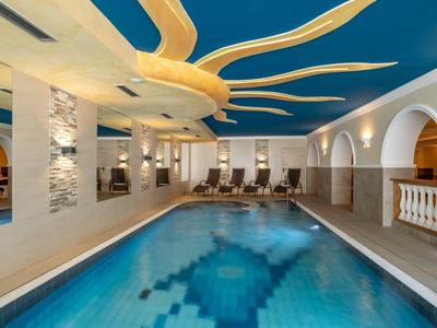 Innenpool mit blauer Decke und bequemen Liegestühlen in einer modernen Hotelanlage.