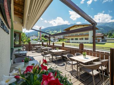 Balkon mit Tischen und Stühlen, Blumen und Bergblick im Hintergrund.