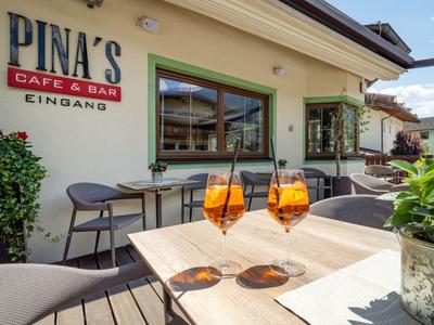 Outdoor-Bereich eines Cafés mit Sonnenterrasse und zwei Orangencocktails auf Holztisch.