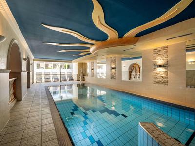 Innenpool mit blauem Deckendekor und bequemen Liegestühlen in einem Hotel.