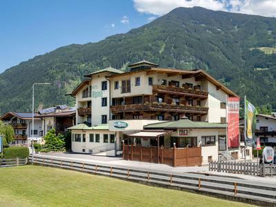Mehrstöckiges Hotel mit Holzverkleidung vor grünen Bergen und blauem Himmel.