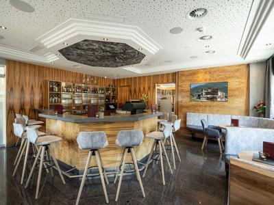 Moderner Hotelbarbereich mit hohem Holzthekenpult und umlaufenden Barhockern in Grau.