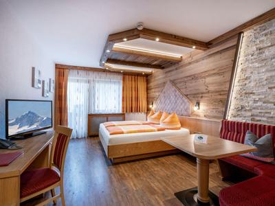Hell eingerichtetes Hotelzimmer mit Doppelbett, Fernseher und Sitzecke.