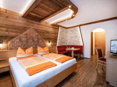 Gemütliches Hotelzimmer mit Doppelbett, Holzwand und Sitzbereich in warmen Farben.