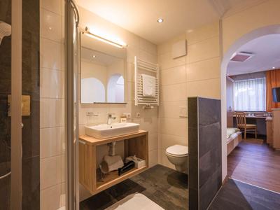 Modernes Hotelbadezimmer mit Dusche, Waschbecken, Toilette und Zugang zum Wohnzimmer.