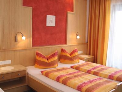 Helles Hotelzimmer mit Doppelbett, Holzmöbeln und bunten Vorhängen.
