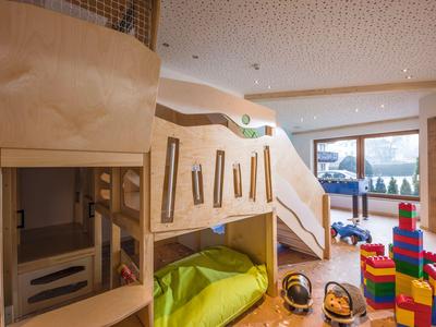 Helles Kinderspielzimmer mit Holzmöbeln, farbigen Bausteinen und großen Fenstern.
