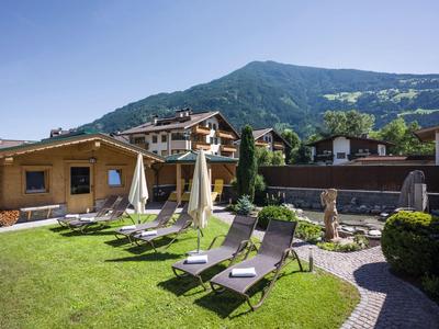 Grüner Garten mit Liegestühlen vor einem Chalet und Bergen im Hintergrund.