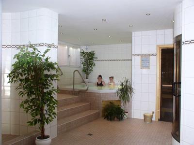 Helles Badezimmer mit weißen Fliesen, Pflanzen und zwei Personen im Whirlpool.