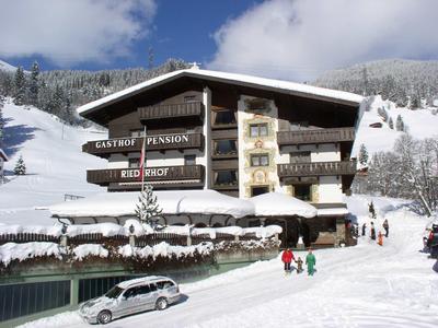 Schneebedecktes Gasthaus in Berglandschaft mit Skifahrern und verschneiten Bäumen im Winter.